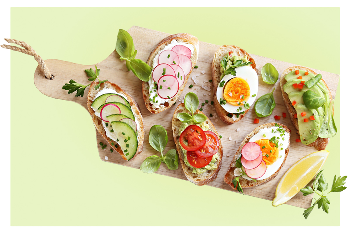Four laughing young adults, two holding a colorful bowl of salad and falafel against an orange background.