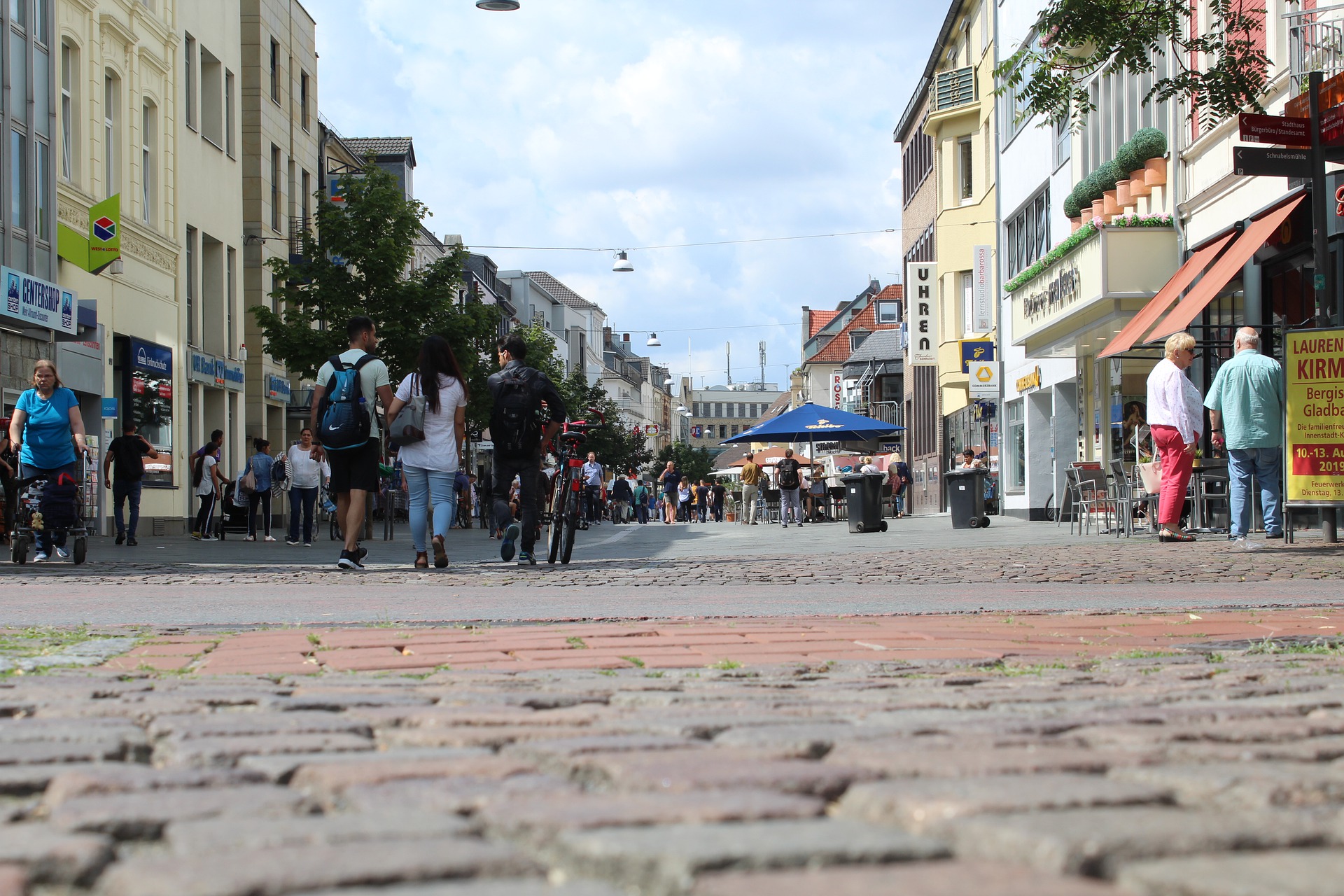 Vier lachende junge Erwachsene, zwei halten eine bunte Schüssel mit Salat und Falafel vor einem orangefarbenen Hintergrund.