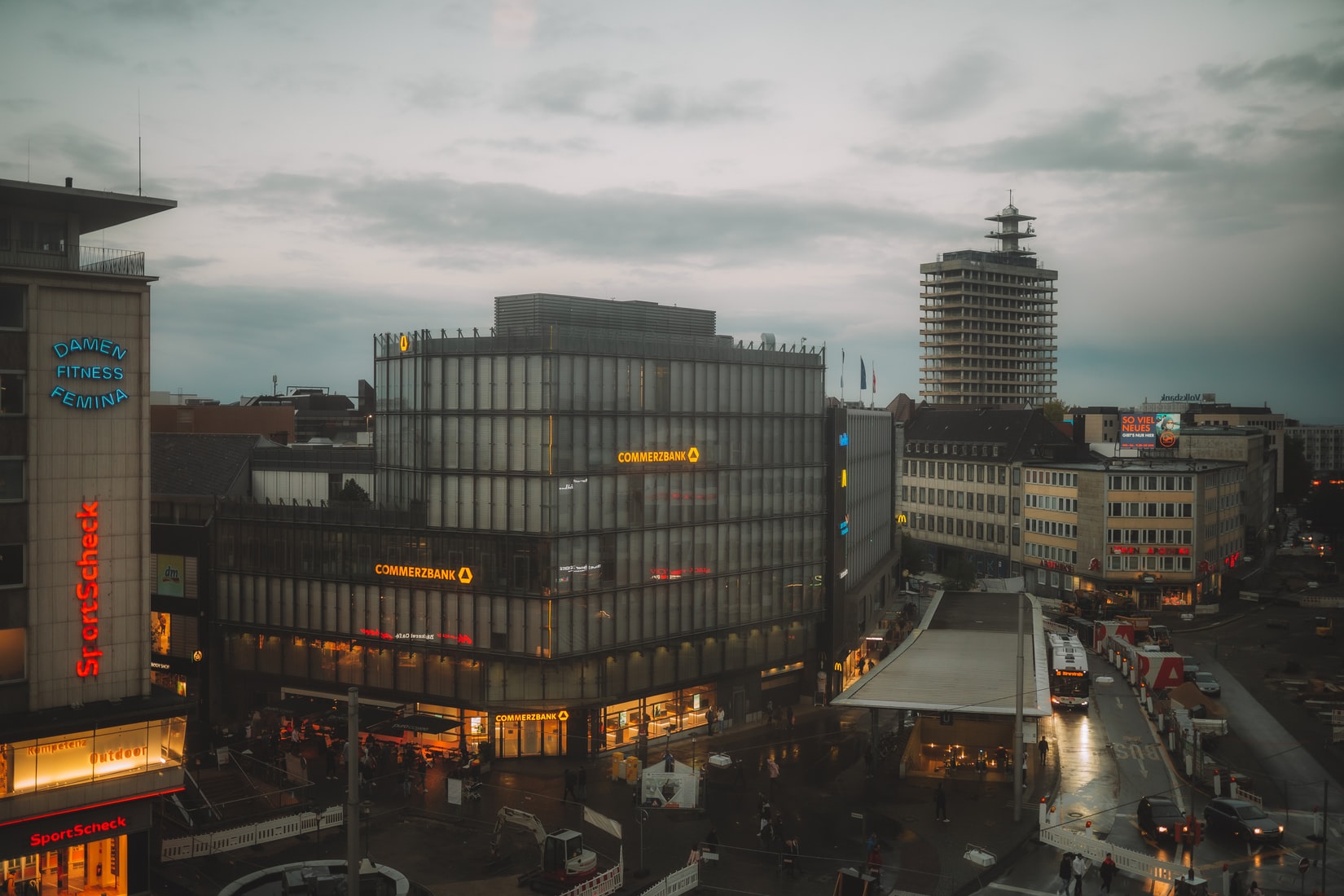 Vier lachende junge Erwachsene, zwei halten eine bunte Schüssel mit Salat und Falafel vor einem orangefarbenen Hintergrund.