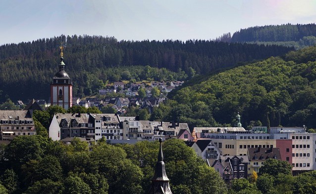 Vier lachende junge Erwachsene, zwei halten eine bunte Schüssel mit Salat und Falafel vor einem orangefarbenen Hintergrund.