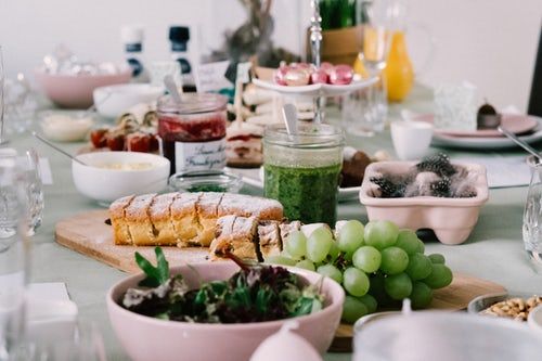 Vier lachende junge Erwachsene, zwei halten eine bunte Schüssel mit Salat und Falafel vor einem orangefarbenen Hintergrund.