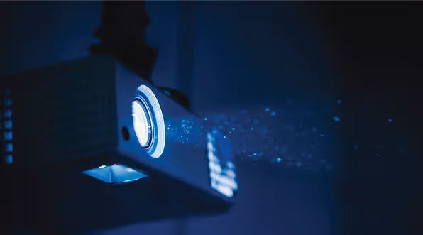 Home cinema projector casting a blue beam of light in a dark room.