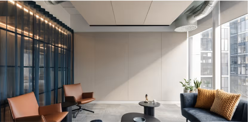 Office lounge with large beige acoustic wall panels, leather chairs and floor-to-ceiling windows.