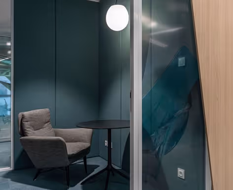Green-toned acoustic meeting pod with felt walls, single armchair and round table.