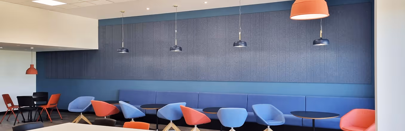 Office cafe with grey felt acoustic wall panels, pendant lights and colourful lounge chairs.