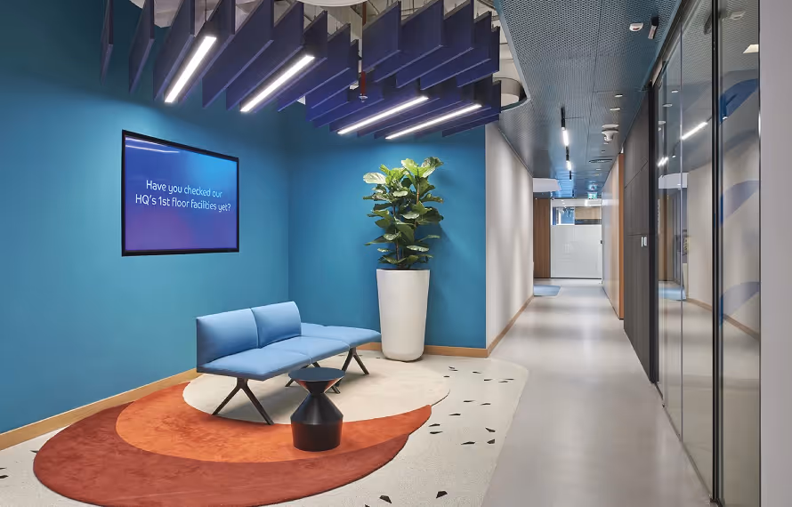 Blue baffle acoustic ceiling treatment above a lounge seating area in an office corridor.