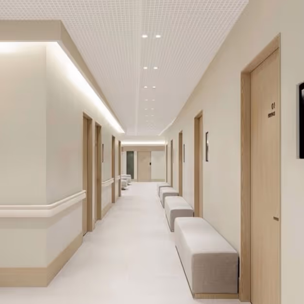 Perforated acoustic ceiling tiles lining a calm clinic corridor with timber doors and bench seating.