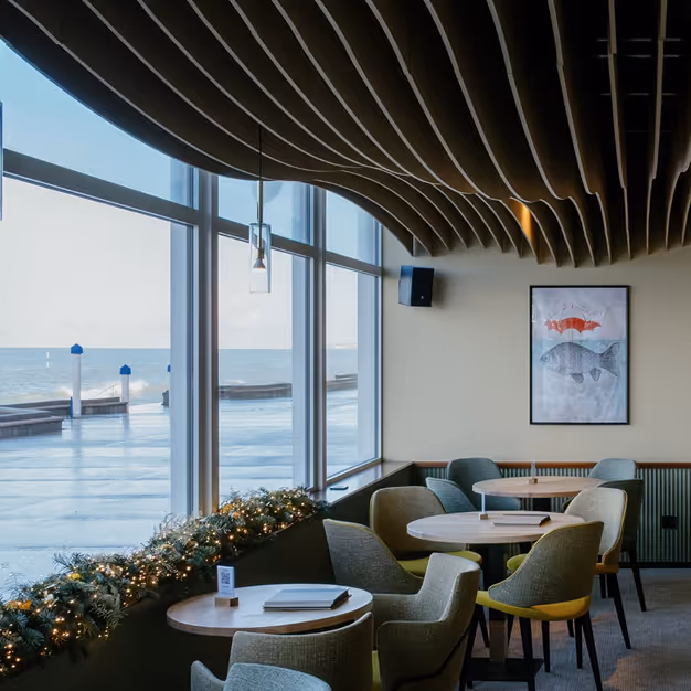Seaside cafe with wave-shaped timber acoustic baffle ceiling and ocean-view seating.
