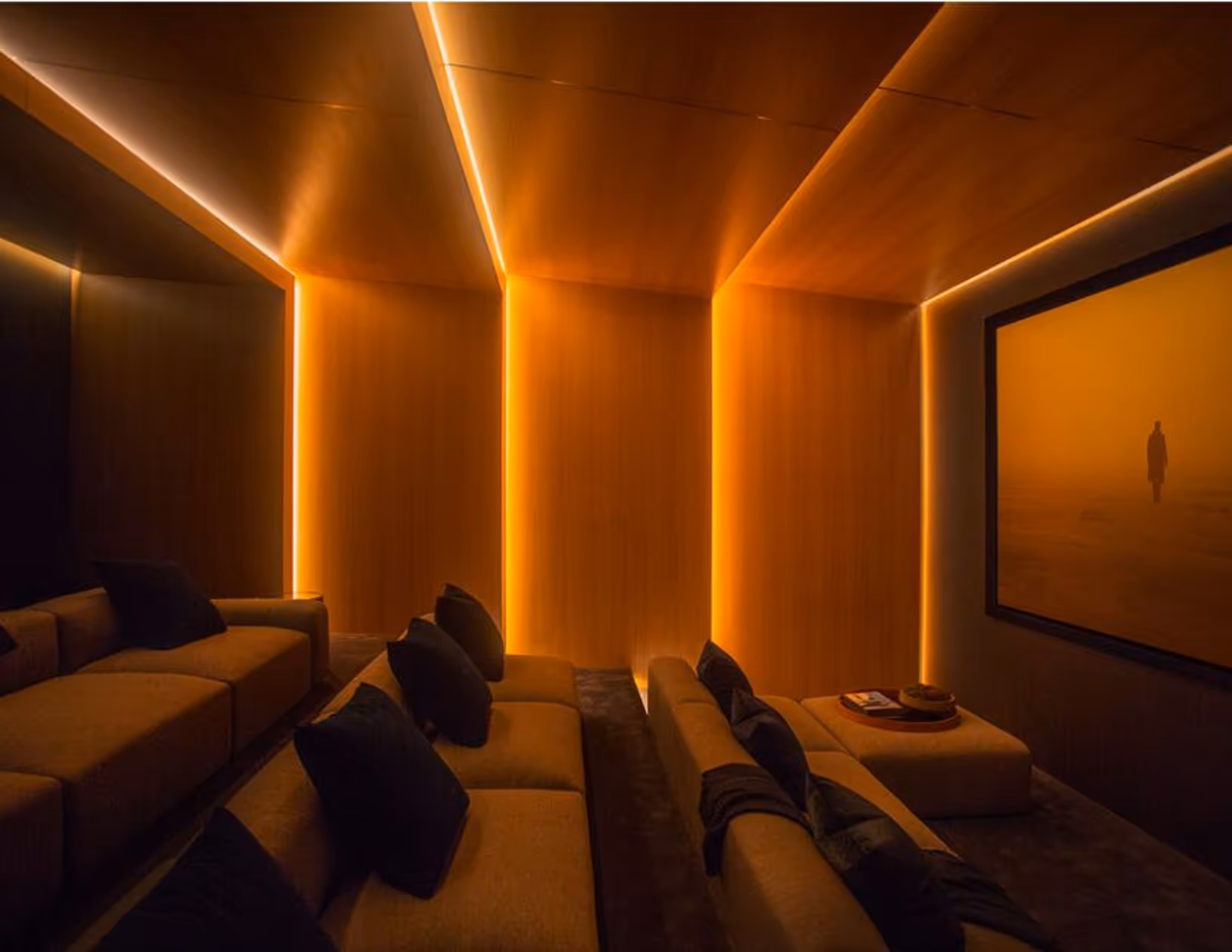 Private cinema with warm backlit acoustic wood walls and tiered sofa seating.