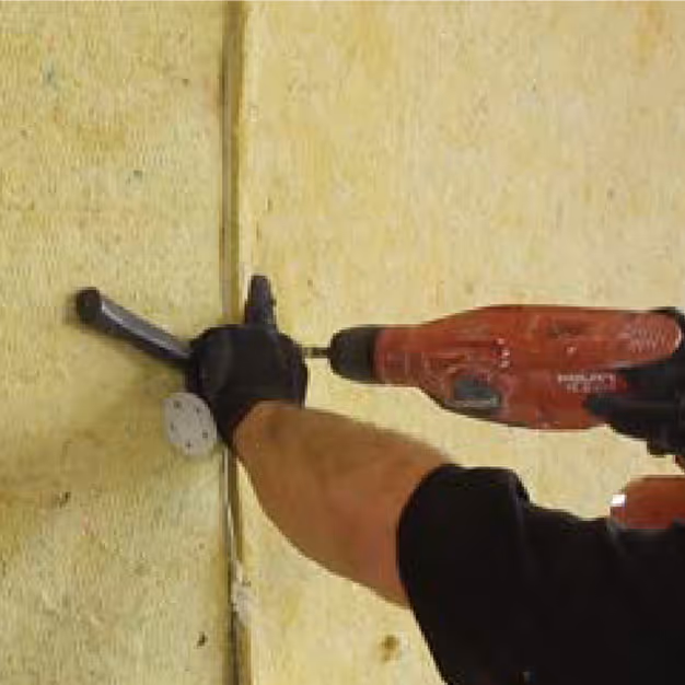Worker drilling mineral wool acoustic insulation into a wall during soundproofing installation.