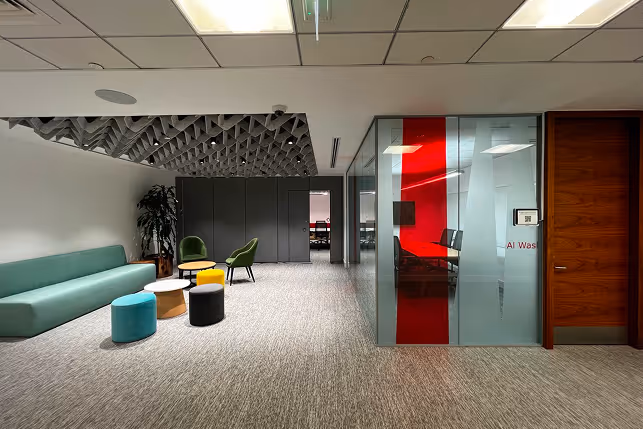 Office lobby with sculptural acoustic baffle ceiling and soft seating in a meeting area.