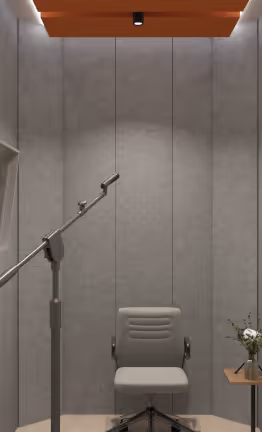 Acoustic recording booth lined with grey felt panels, a microphone stand, and chair.