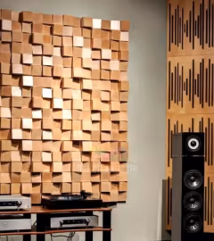 Wooden 3D acoustic diffuser panel on a listening-room wall beside floor-standing speakers.
