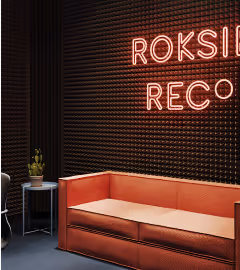 Red office lounge with neon signage and a perforated acoustic wall behind a sofa.