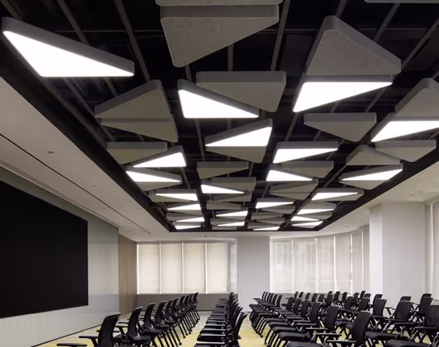 Black and grey circular acoustic ceiling rafts above an open-plan office workspace.