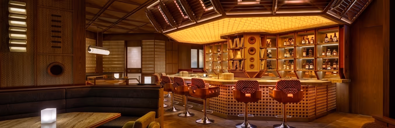 Warm wood-clad restaurant bar with a backlit acoustic ceiling and bar stools.