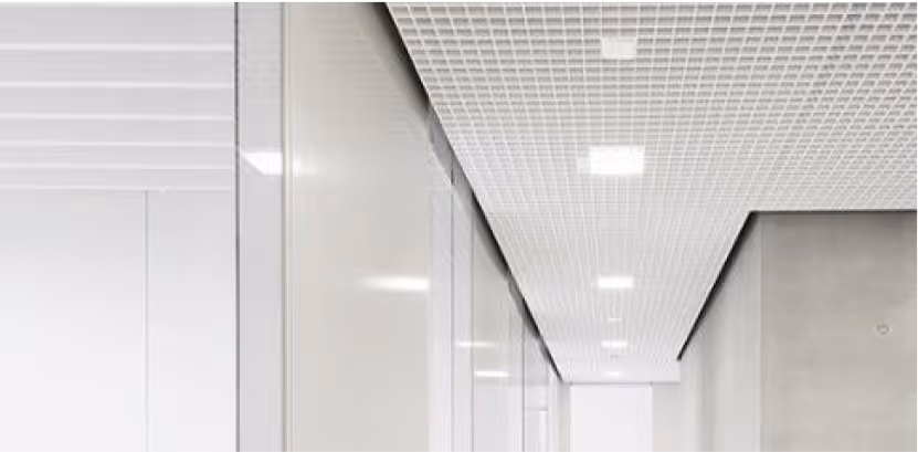 White perforated acoustic ceiling running down a bright office corridor.