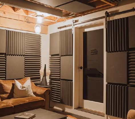 Basement studio lounge with grey acoustic foam wall panels, a leather sofa and sliding door.
