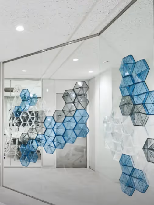 Blue translucent geometric acoustic diffuser modules mounted on a glass office wall.