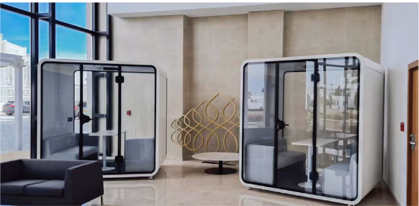 Office lobby with two freestanding acoustic phone booths, a sofa and a gold sound-diffuser sculpture.