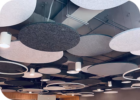 Round grey and white acoustic ceiling discs suspended above ceiling downlights.