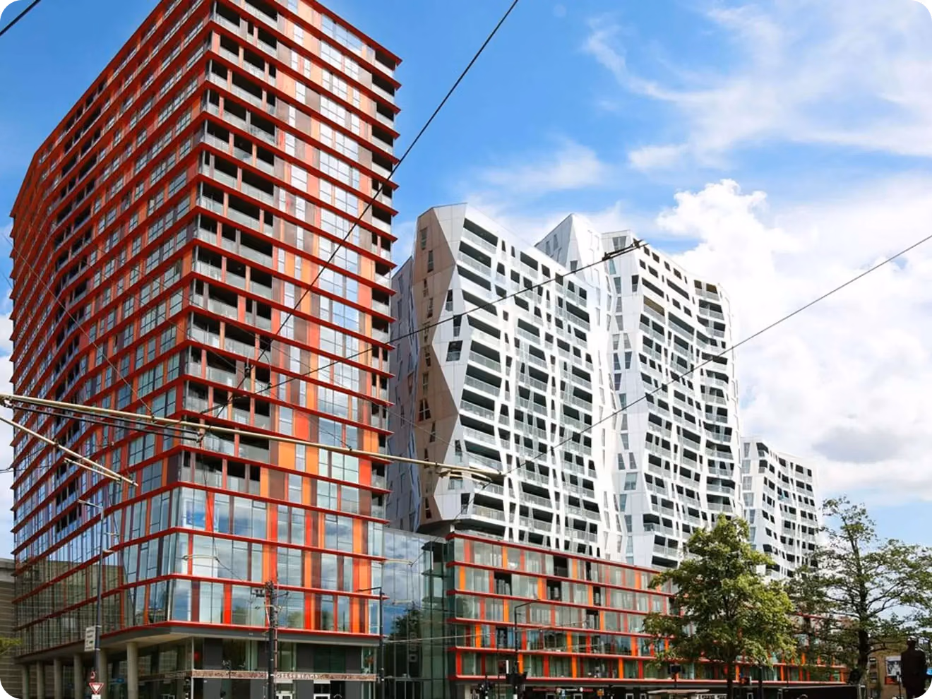 Modern multi-story buildings with red accents and white geometric-patterned facade under a blue sky with clouds.