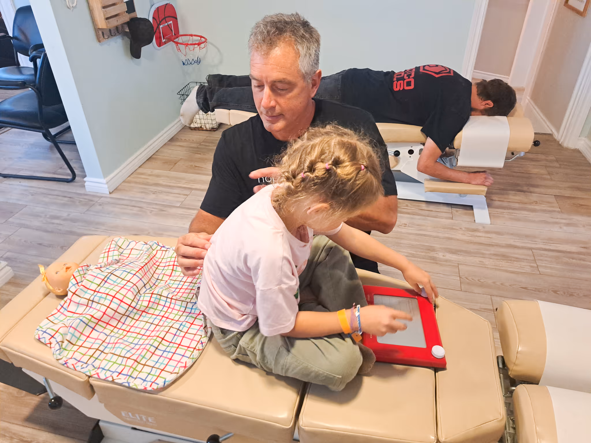Man in blue shirt holding a baby in pink clothes next to a smiling young girl wearing a pink cap and floral dress.