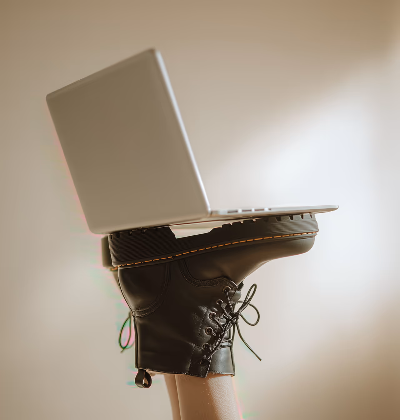 A closed silver laptop balanced on the soles of black leather boots worn by raised legs.