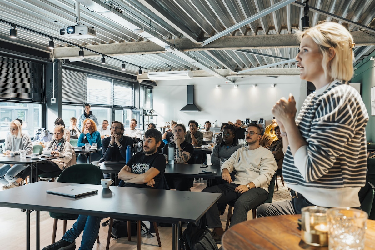 Grupo diverso en clase, mujer rubia presentando frente a estudiantes sentados