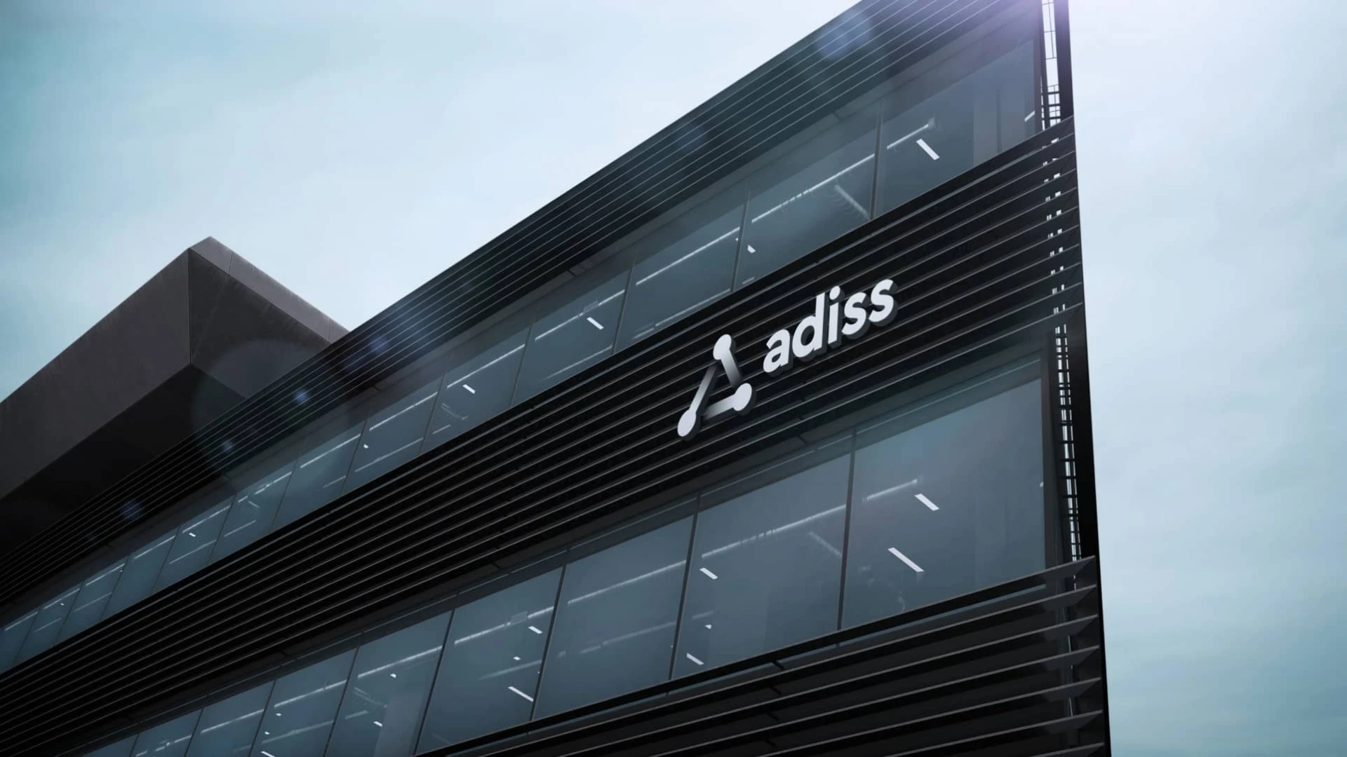 Vista en contrapicado de un edificio corporativo moderno con fachada de vidrio oscuro, mostrando el logotipo de "adiss" en letras blancas junto a un símbolo triangular estilizado en la parte superior