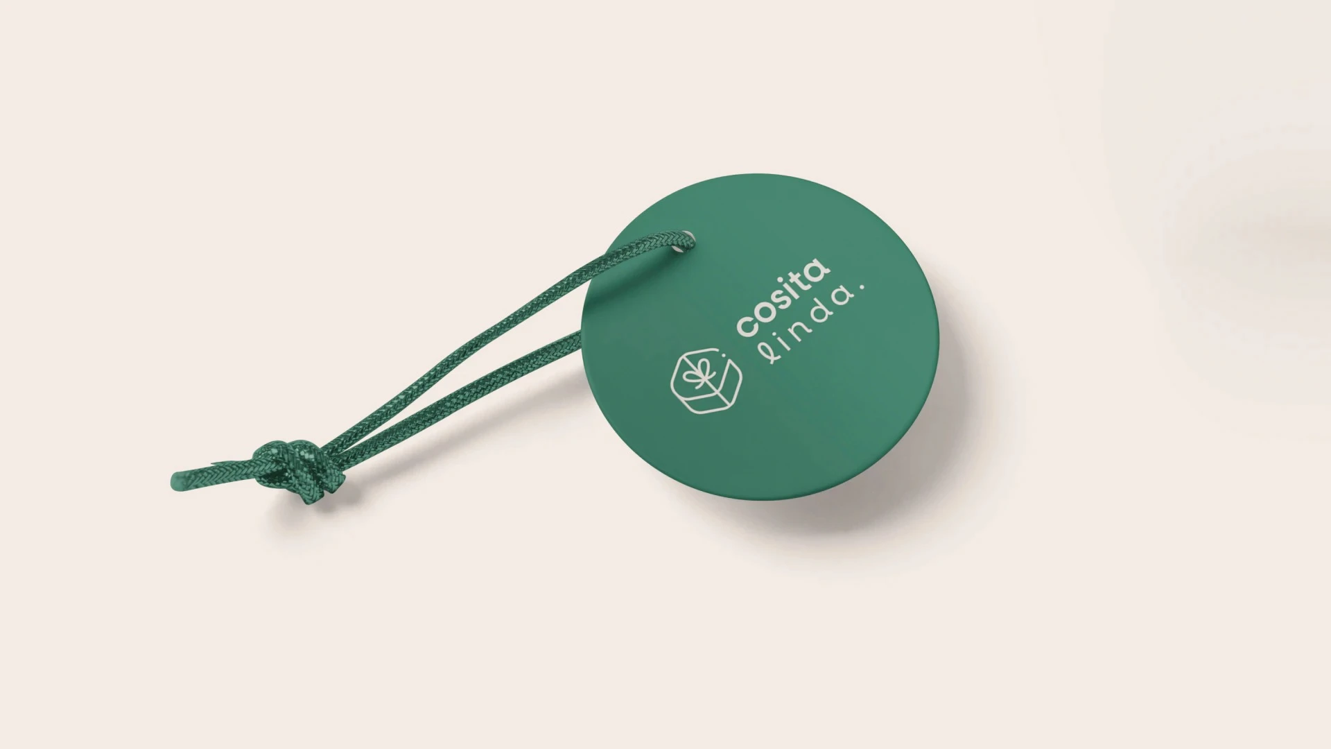 Etiqueta redonda de color verde oscuro con un cordón anudado, presentando el logotipo y el ícono de regalo de Cosita Linda, en color crema sobre un fondo neutro