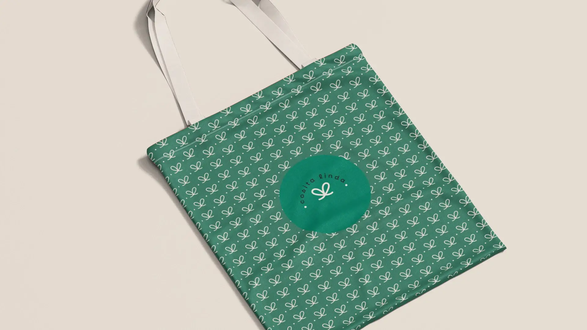 Mockup de bolsa de tela tote bag verde estampada con patrón repetitivo de lazos blancos y el logotipo circular de la marca Cosita Linda al centro