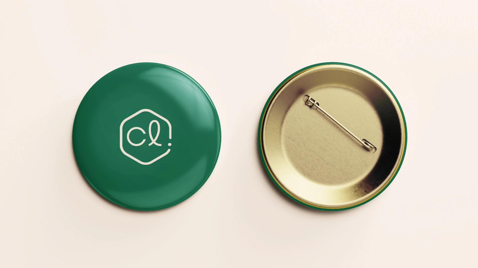Dos botones circulares tipo chapa sobre fondo beige: a la izquierda, el anverso verde oscuro brillante con el logotipo en un hexágono blanco; a la derecha, el reverso metálico dorado mostrando el alfiler de sujeción