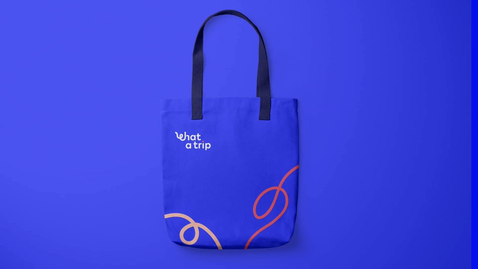 Bolsa tote de tela color azul eléctrico sobre fondo del mismo tono, decorada con el logotipo de 'What a Trip' en blanco en la parte superior y trazos ondulados abstractos en amarillo y rojizo en la base