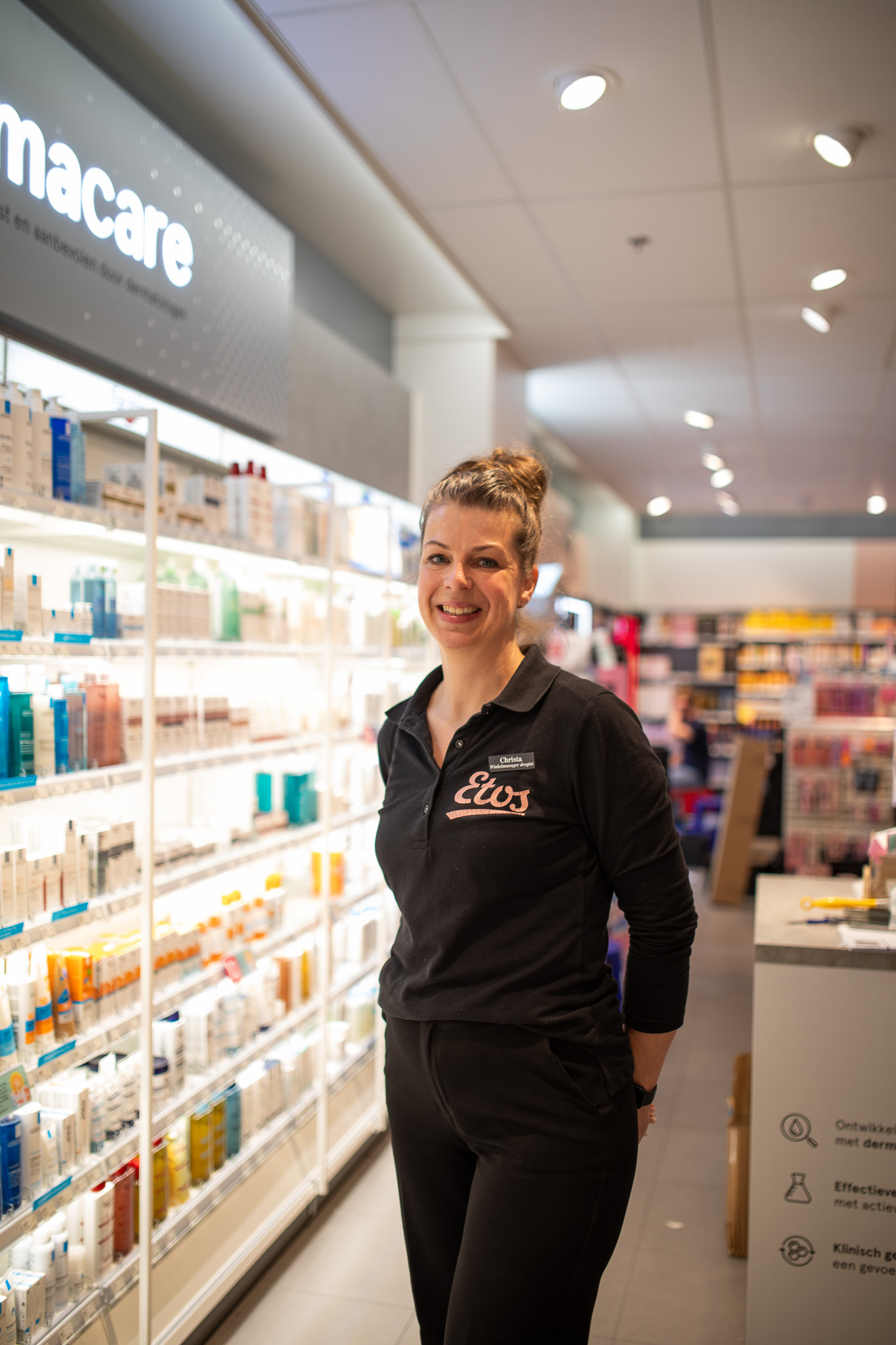 Vrolijke vrouwelijke medewerker van Etos staat in winkelgang met huidverzorgingsproducten op de achtergrond.