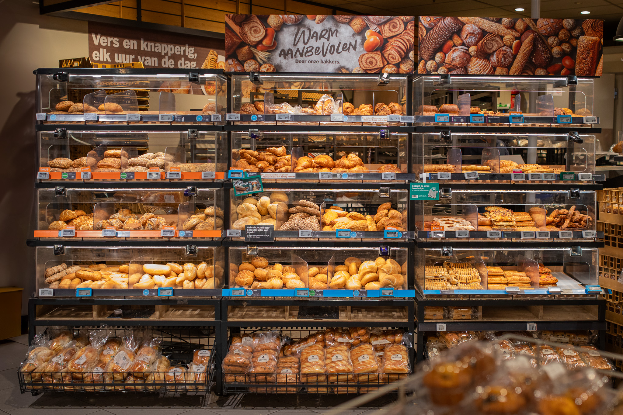 Bakwand in een supermarkt met diverse verse broden, croissants en gebak verpakt in doorzichtige vakken.