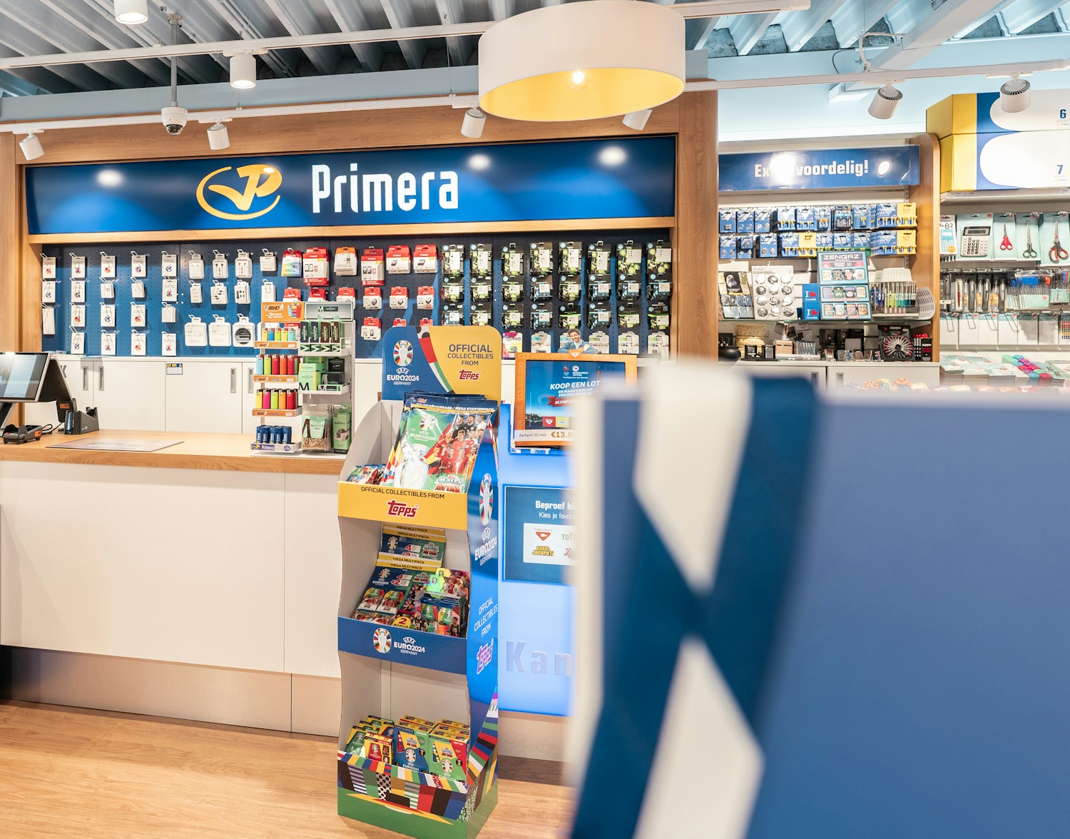 Interieur van een Primera-winkel met een balie, displays met briefpapier, en officiële Euro 2024 verzamelkaarten.
