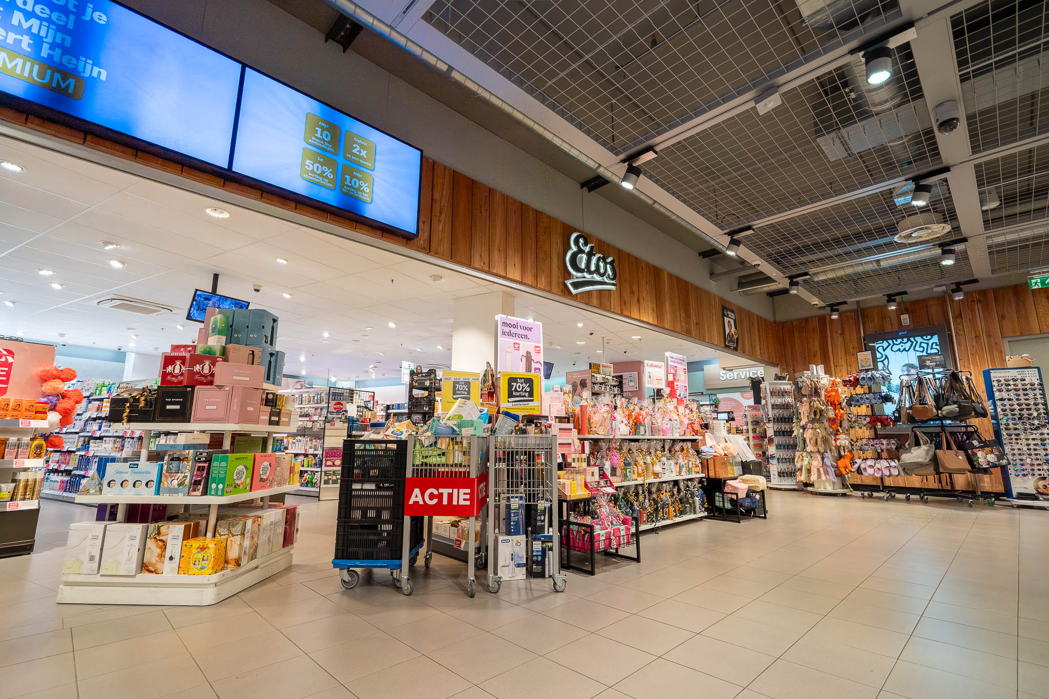 Interieur van een Etos winkel met schappen vol producten, kortingsborden en tassen aan rekken.