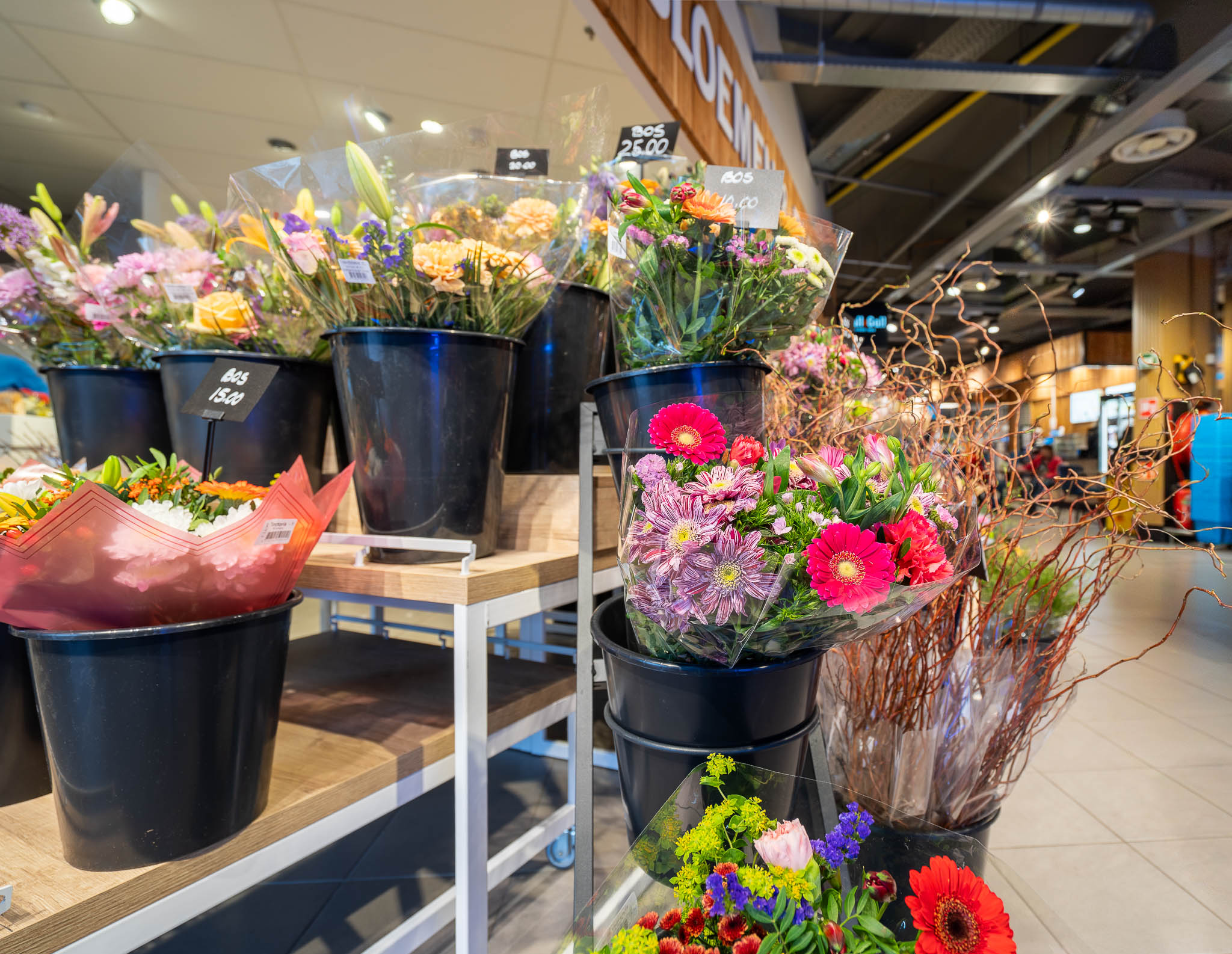 Een winkelinterieur met verschillende kleurrijke bloemenboeketten in zwarte emmers op houten en metalen rekken.