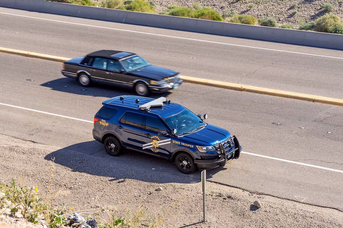 Nevada Highway Patrol SUV parked on roadside next to a black sedan driving on highway.