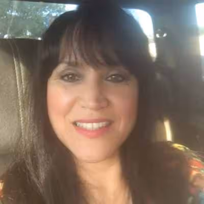 Smiling woman with long dark hair sitting in a car with sunlight on her face.