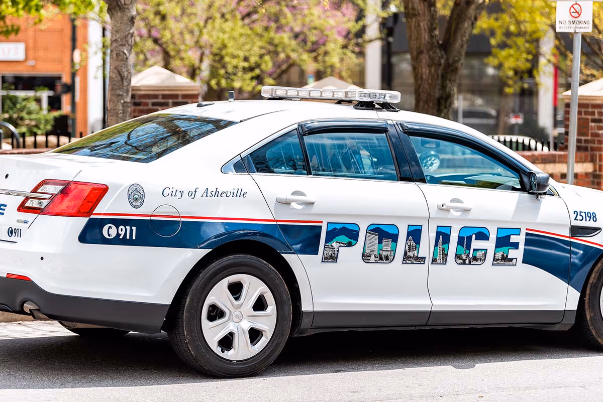 White City of Asheville police car parked on street with blue stripe and cityscape lettering.