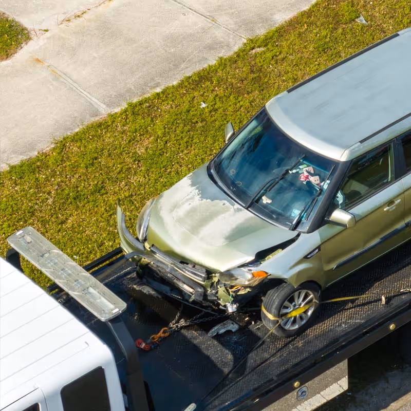 Damaged silver car with front-end collision secured on a tow truck bed.