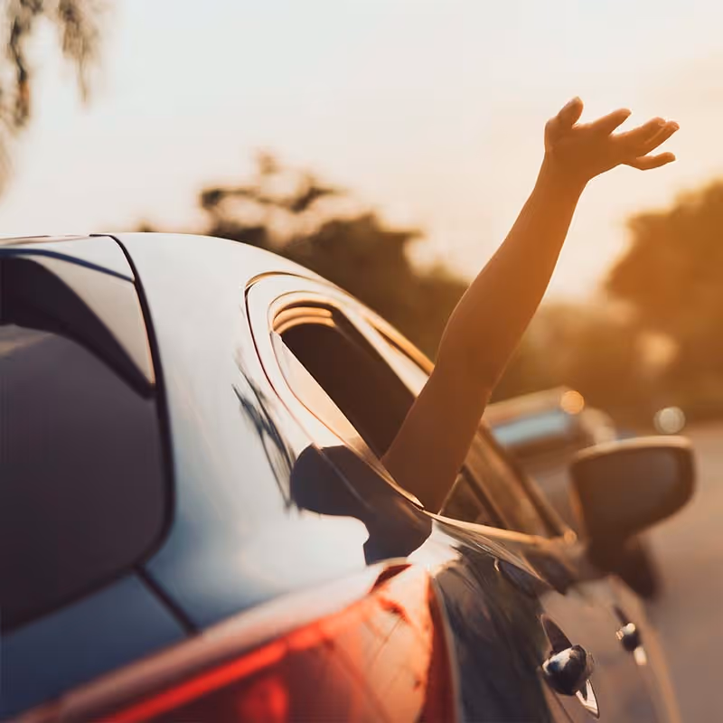 Arm extended out of a car window during a sunset drive on a road with blurred background.