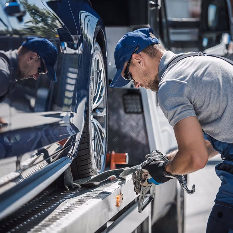 Tow truck driver securing a strap around a car tire on the truck bed.