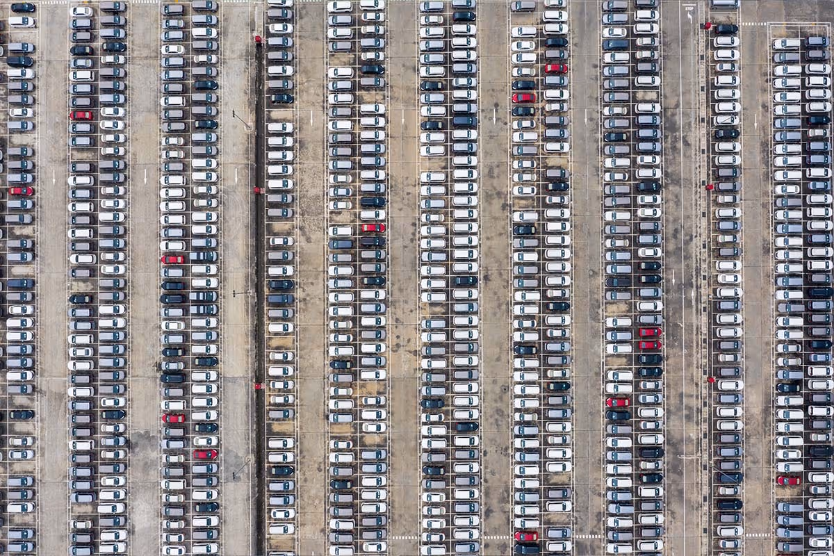 Aerial view of a large impound lot with rows of tightly parked white, black, and red cars.