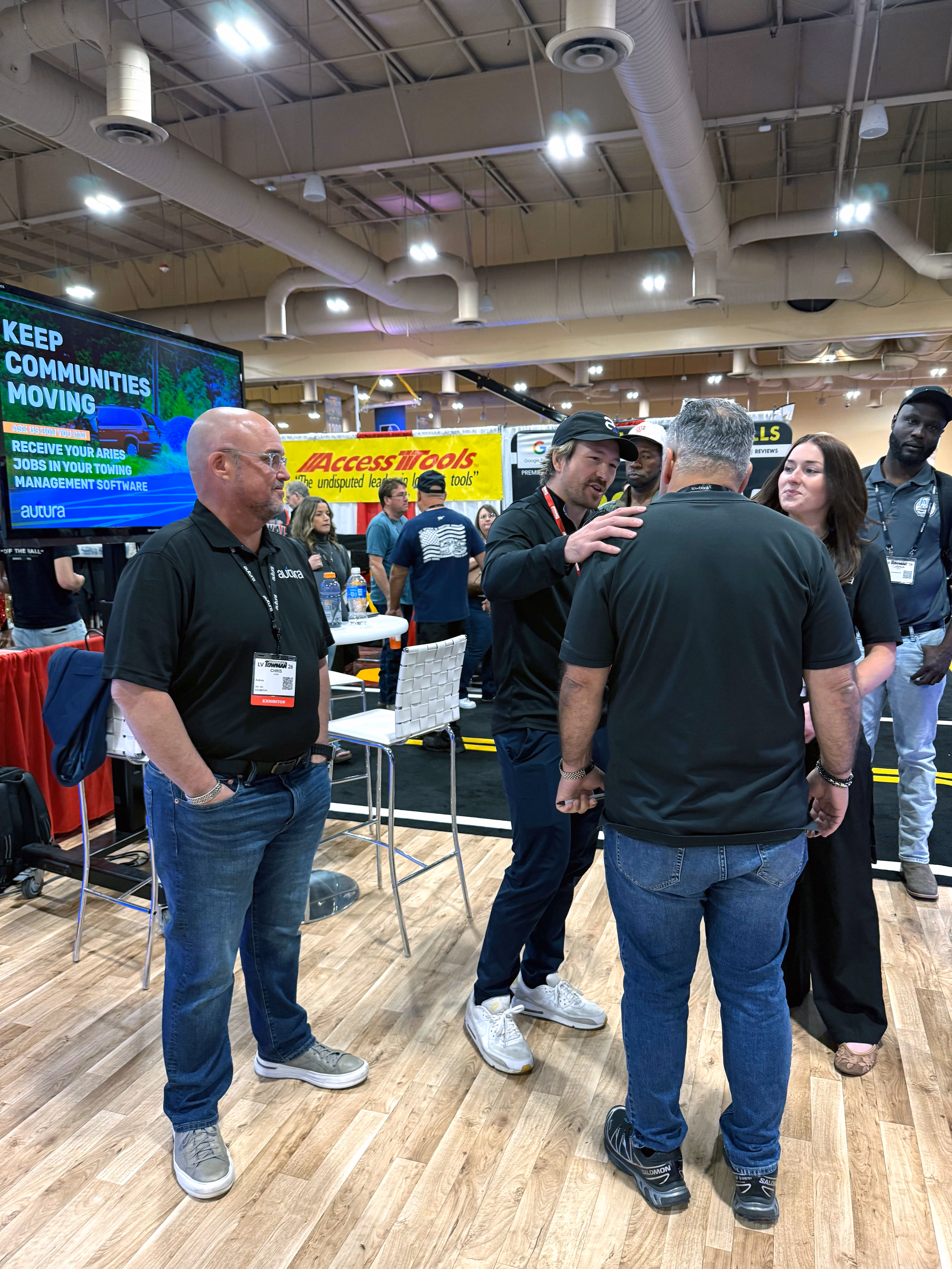 Group of five people chatting at a trade show booth with a digital display and promotional banners.