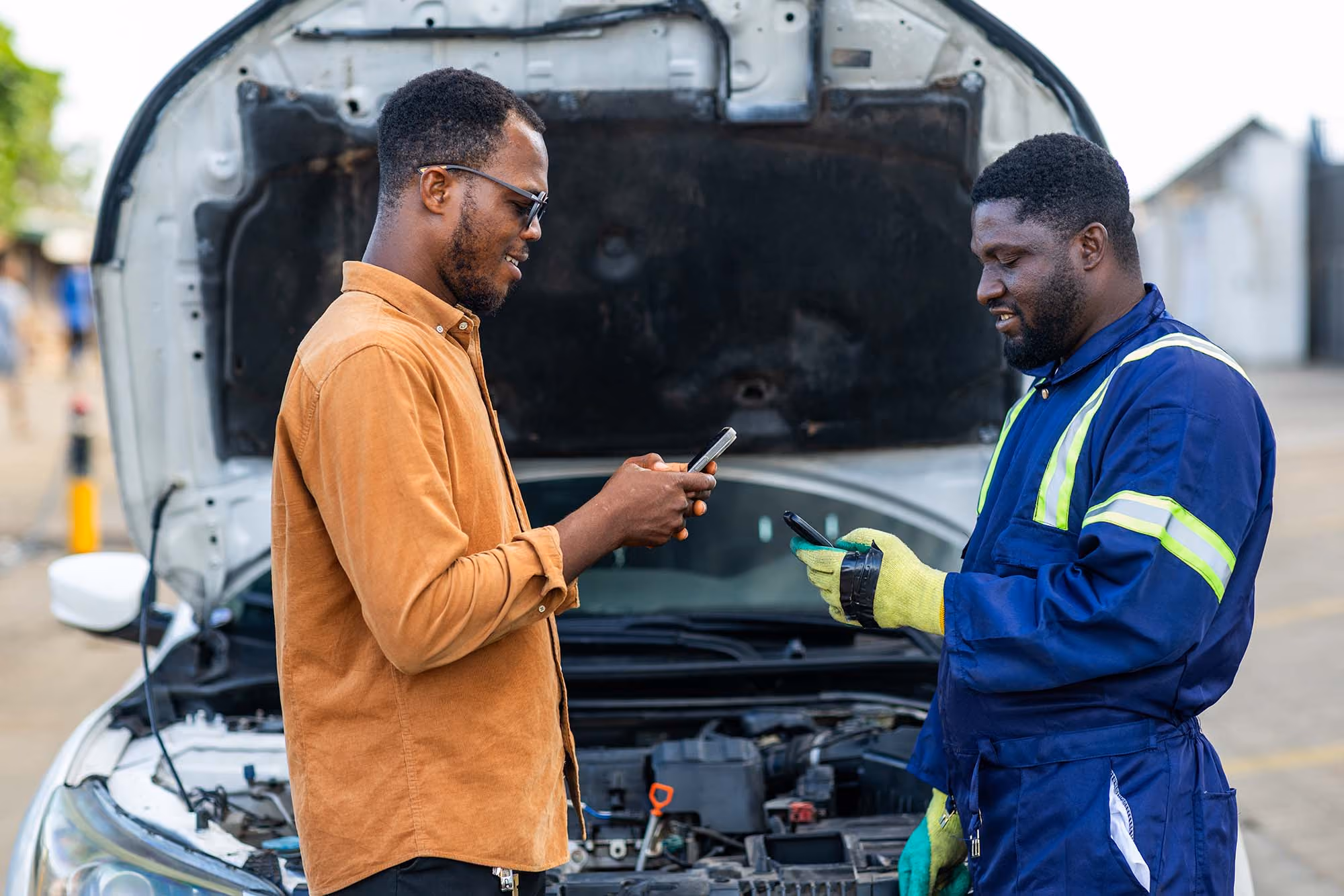 Man paying a tow truck driver using his phone while standing in front of a broken down car