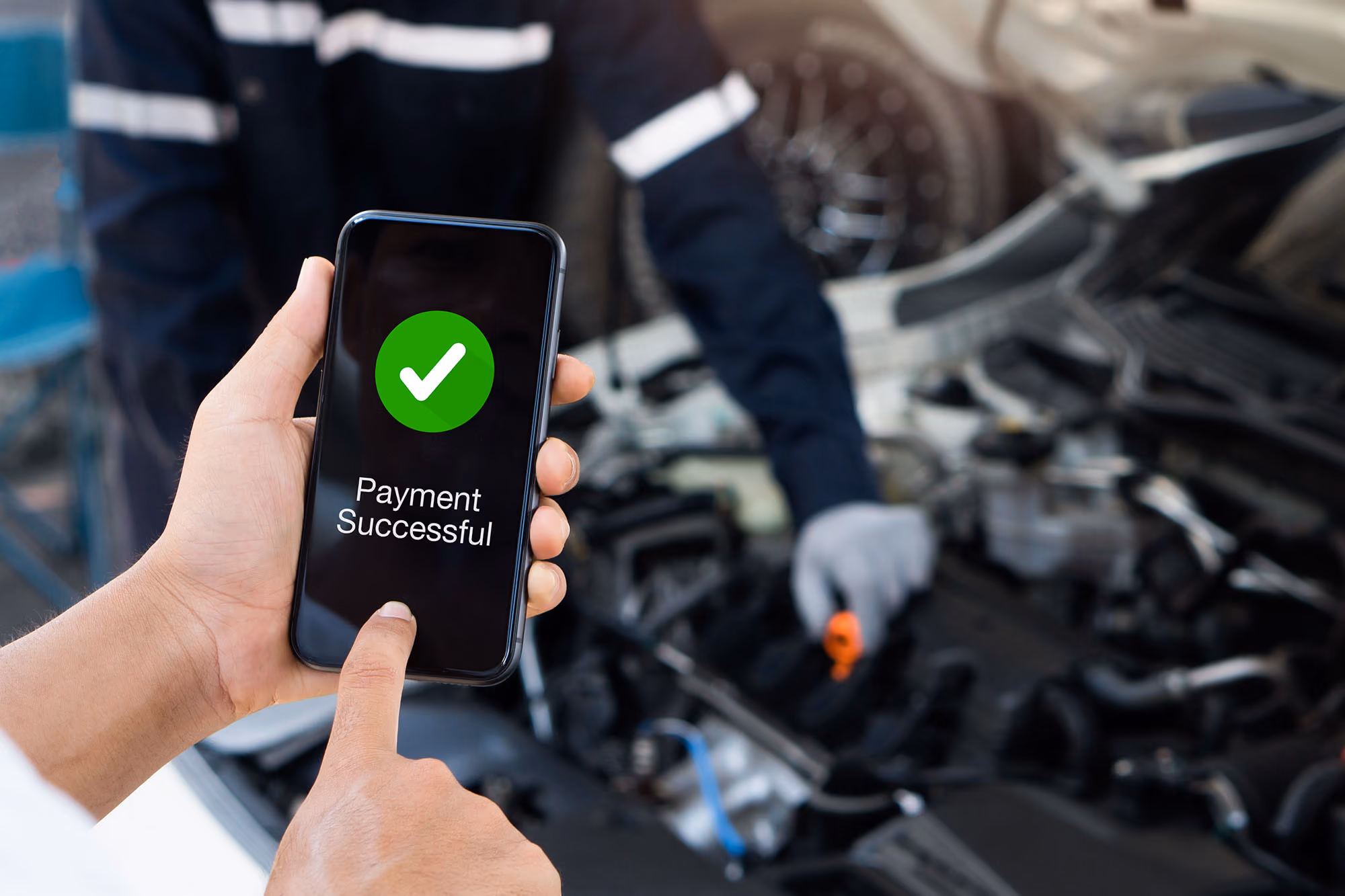 Phone displaying Payment Successful held in someone's hand in front of car mechanic and open car hood