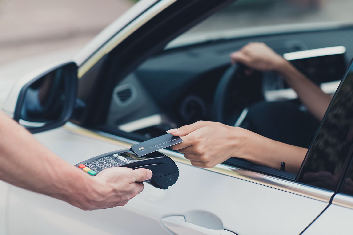 Woman tapping credit card to a mobile payment terminal from her car